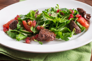 Warm salad with fried chicken liver and pomegranate seeds. Wooden background