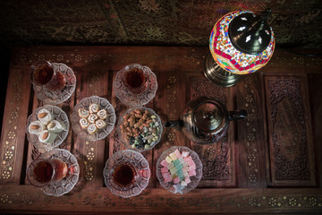 Arabian tea in glass with eastern snacks on vintage wooden surface. Eastern tea concept. Low light lounge interior with carpet. Empty space.