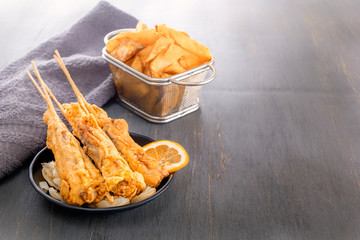 baked fish on skewers in a black plate and french fries on a wooden table. Copy space