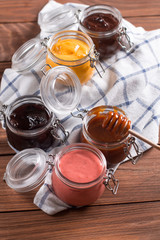 Natural creams in a small glass jar on a wooden table. Caramel, mango, strawberry, berry, chocolate sauce