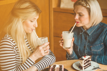 Two happy women sitting in a cafe, drink a cocktail, tell each other funny stories, being in a good mood, laughing happily