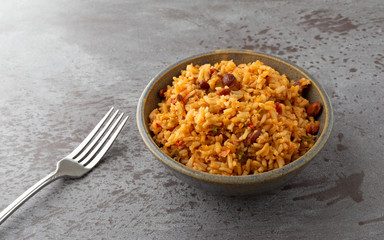 Side view of a bowl of Mexican rice and beans with a fork to the side on a gray background