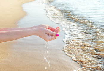 Woman's hands holding water in palms at sea beach.