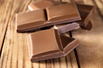 Pieces of chocolate bar on wooden table. Close up.