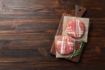 Hamburger raw cutlets with rosemary on cutting board and wooden table