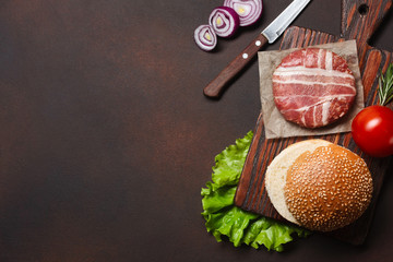 Hamburger ingredients raw cutlet, tomatos, lettuce, bun, cheese, cucumbers and onion on rusty background