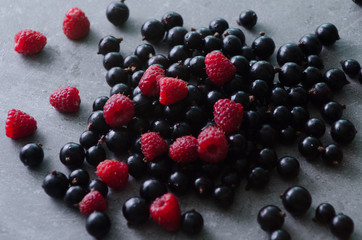 Bunch of fresh raspberries and black currants on a grey table. Close-up view