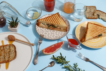 Appetizing turkey sandwich on colored plates in the composition of the server table with a glass of water, tomato juice, sauce and grapefruit pieces. Top view. Breakfast concept.