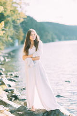 Fototapeta na wymiar Girl in boudoir dress on the lake, standing and smiling. Unity with nature, morning bride in Russia. Beautiful eyes and model appearance