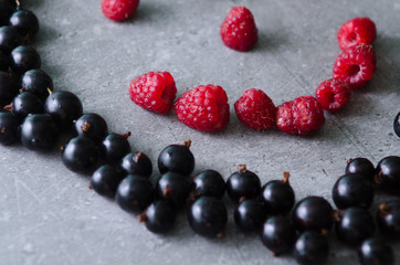 Bunch of fresh raspberries and black currants on a grey background. Close-up view