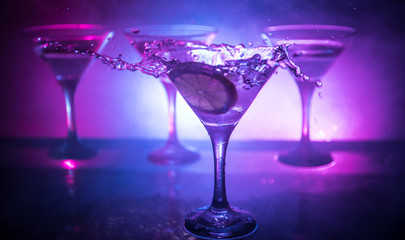 Martini cocktail glass in hand splashing on dark toned smoky background or colorful cocktail in glass with splashes and olives. Party club entertainment. Mixed light. Selective focus