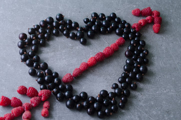 Black currants and raspberries in a shape of heart and arrow on a grey kitchen table