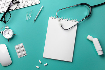 Stethoscope in doctors desk with keyboard, alarm clock, glasses, inhaler, syringe, ampoules, inhaler and pills