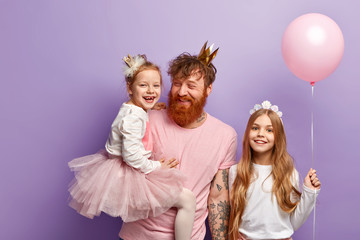 Isolated shot of friendly family celebrate birthday. Affectionate father with thick red beard laughs joyfully, plays with small daughters during party. Family holiday concept. Fathers birthday