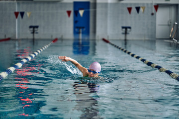 Female athlete swimming fast in crawl style.  Splashes of water scatter in different directions.