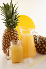 Jug and glass of pineapple juice with fruits on white background.
