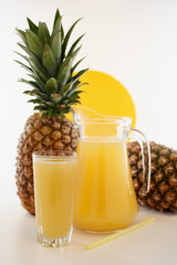 Jug and glass of pineapple juice with fruits on white background.