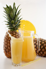 Jug and glass of pineapple juice with fruits on white background. Splash yellow drink. 
