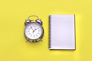 Vintage alarm clock next to a notepad on a yellow background