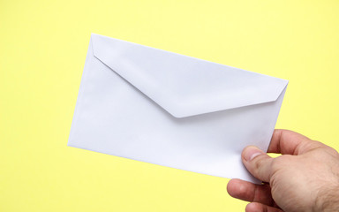 A hand is holding a white envelope on a yellow background.
