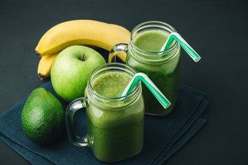 Green, healthy, detox smoothie from avocado, banana, apple in mason jar on blue napkin, dark background, vegetarian food