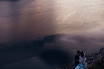 river water with reflection. Newlyweds hug on the rocky shore of