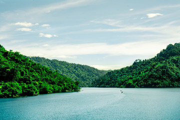 Fototapeta premium Beautiful landscape view of green mountain beside river on bright sky clouds, Water storage dam, Green tree nature mountain on riverside