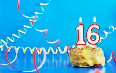 Birthday of sixteen years. Cupcake with white burning candle in the form of number 16. Vivid blue...