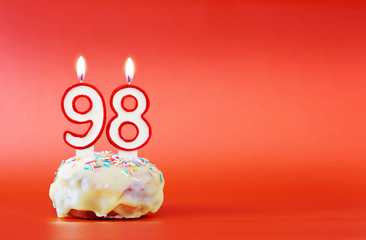 Ninety eight years birthday. Cupcake with white burning candle in the form of number 98. Vivid red background with copy space
