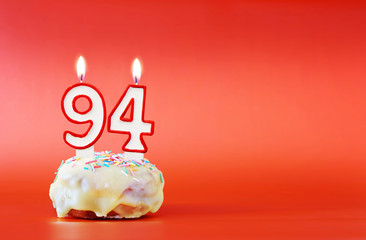 Ninety four years birthday. Cupcake with white burning candle in the form of number 94. Vivid red...