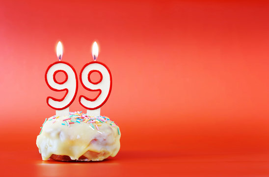 Ninety nine years birthday. Cupcake with white burning candle in the form of number 99. Vivid red background with copy space