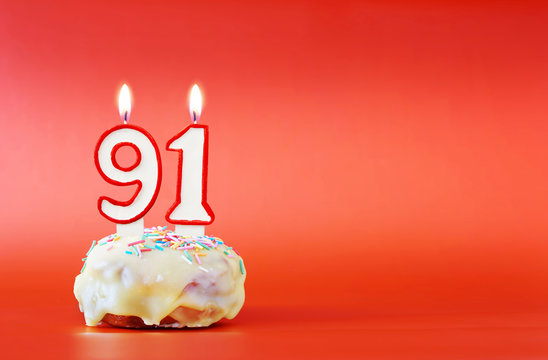 Ninety one years birthday. Cupcake with white burning candle in the form of number 91. Vivid red background with copy space