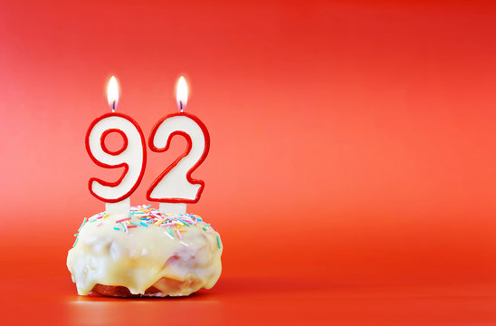 Ninety two years birthday. Cupcake with white burning candle in the form of number 92. Vivid red background with copy space