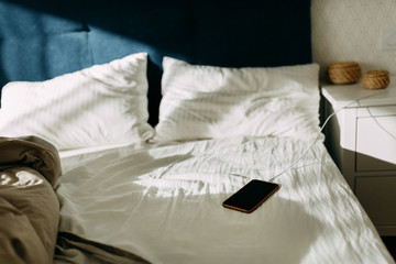 Morning light on the pillows, empty bed and unmade at the first light of dawn, battery mobile phone...