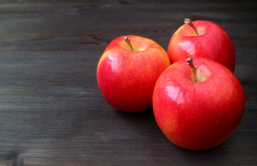  Three red apples on dark colored wooden table with free space for text and design  