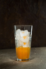 Half a glass of orange juice with ice cubes on a dark background. Selective focus.