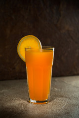 Glass of orange juice and slices of oranges on a dark background. Selective focus.