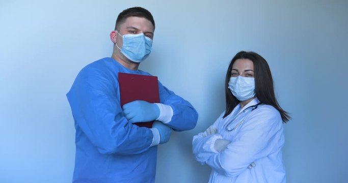 In the hospital (clinic) Two young doctors in lab coats a nurse and a doctor with a folder in their hands, scratching the synchron hands. Concept of: Medical mask, Medical gloves, Man, Woman.