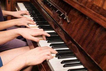 Brother and sister play at four hands on the piano at home and study a new musical piece