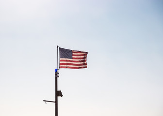 American flag flying in the wind against a clear, hazy blue sky