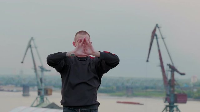 Slow motion shoot of a talented young dancing man performing various freestyle vogue dance on the industrial roof. Construction cranes on the background