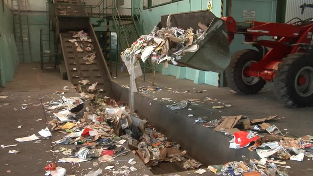 Loader loading waste paper on a conveyor belt.