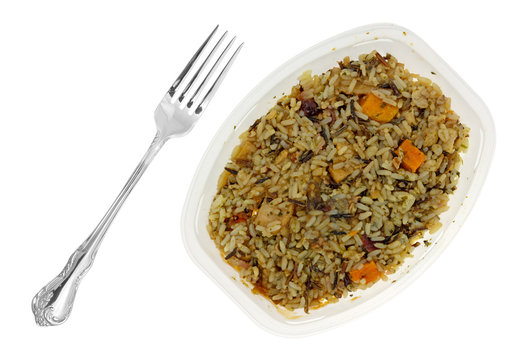 Chicken with pecans and wild rice TV dinner in a plastic tray with a fork to the side isolated on a white background