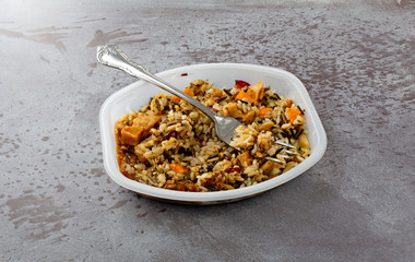 Chicken with pecans and wild rice TV dinner in a plastic tray with a fork to the side on a gray background