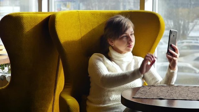 Beautiful woman taking a selfie on her smartphone while sitting in a cafe. Business lunch. Slow motion