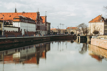 Obraz premium Cityscape of Wroclaw on a sunny spring day. Water of Odra river reflecting gray-blue sky and old classical buildings with red roofs. 