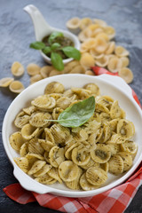 Orecchiette pasta with green basil pesto and grated parmesan served in a white plate, vertical shot