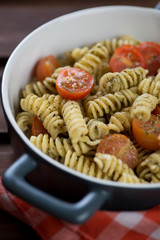 Close-up of fusilli served with basil pesto sauce and cherry tomatoes, vertical shot