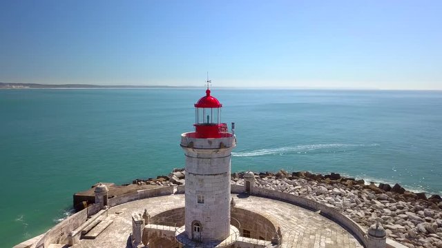 Aerial, orbit, drone shot, around Bugio lighthouse, on a rocky island, a boat bypassing , on the atlantic ocean, on a sunny day, near Oeiras coast and Tejo river, in Lisbon, Portugal