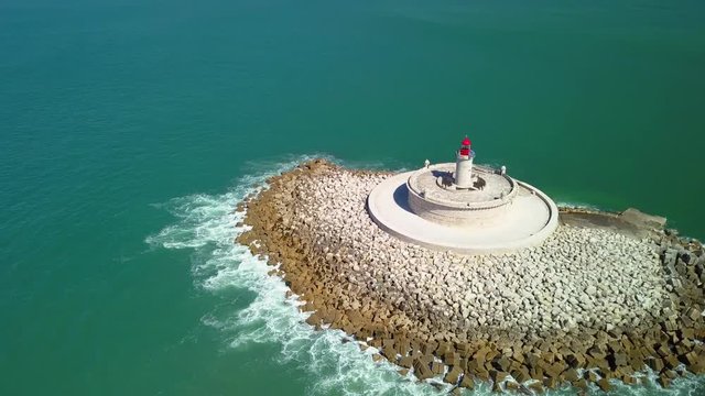 Aerial, orbit, drone shot, tilting up around Bugio lighthouse, on a rocky island , on the atlantic ocean, on a sunny day, revealing the Oeiras coast, near Tejo river, in Lisbon, Portugal